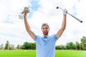 Happy winner. Happy male golfer holding trophy and driver while standing on golf course photo
