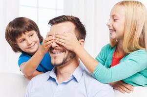 adivina quiénes son dos niños juguetones que cubren los ojos de su alegre padre y sonríen foto