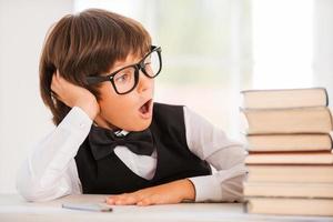 sus libros favoritos. niño emocionado con camisa y corbata de moño sentado en la mesa y mirando la pila de libros foto