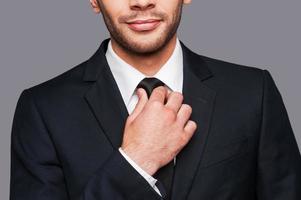 confianza de cuello blanco. primer plano de un joven con ropa formal ajustando su corbata mientras se enfrenta a un fondo gris foto