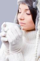 Winter dreaming. Close-up of young women in warm winter clothing drinking coffee and keeping eyes closed while standing against grey background photo