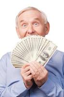 I am rich Portrait of happy senior man covering his mouth by money and looking at camera and while standing against white background photo