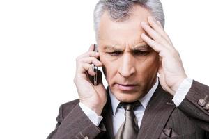 Unexpected bad news. Portrait of frustrated mature man in formalwear holding the mobile phone while standing against white background photo