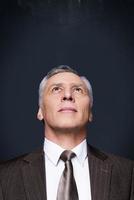 Curious businessman. Portrait of curious senior man in formalwear looking up while standing against blackboard photo