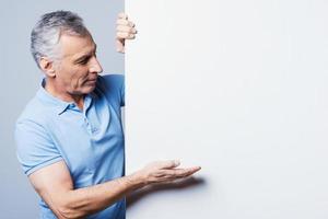 Pointing to your advertisement. Handsome senior man pointing on copy space while standing against grey background photo