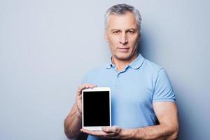 copie el espacio en su tableta. un anciano confiado que muestra su tableta digital y sonríe mientras se enfrenta a un fondo gris foto