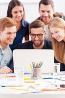 Working as team. Group of cheerful business people in smart casual wear looking at the laptop together and smiling photo