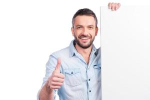 Good product Happy mature man in casual wear leaning at copy space and showing his thumb up while standing against white background photo