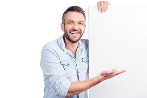 Just look at this perfect proposition Happy mature man in casual wear leaning at copy space and pointing it while standing against white background photo