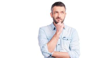 Feeling uncertain about Frustrated young man in casual wear holding hand on chin and looking away while standing isolated on white background photo