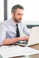 Businessman at work. Confident mature man in shirt and tie working at laptop while sitting at his working place photo