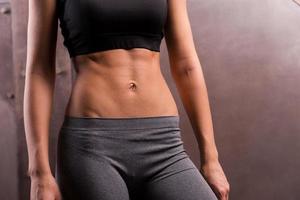 Perfect torso. Close-up of muscular young woman posing with naked torso while standing against metal background photo