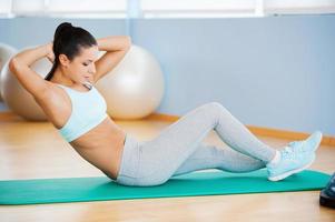 Training her abs. Beautiful young woman in sports clothing exercising while lying on exercise mat photo