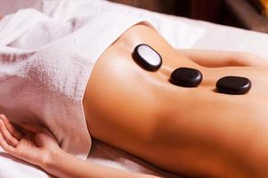 Stone treatment. Top view of young woman with shiny skin lying on front with spa stones on her back photo