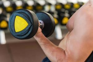 Working at his perfect biceps. Close-up of muscular man working at his biceps while exercising with dumbbells in gym photo