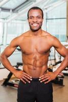 Strong and healthy. Confident young African man holding hands on hip and smiling while standing in gym photo