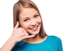 I am waiting for your call Cheerful young women gesturing phone sign and smiling while standing against white background photo