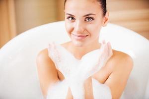 Bubble fun. Top view of attractive young woman blowing soap bubbles from her hands and smiling while enjoying luxurious bath photo