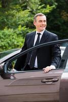 This car is perfect for me. Cheerful mature man in formalwear looking away and smiling while getting out from car photo