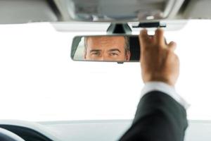 Man adjusting car mirror. Close-up of mature man in formalwear adjusting mirror while sitting in his car photo