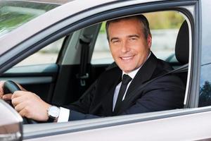 Feeling comfortable in his new car. Cheerful mature man in formalwear driving car and smiling photo