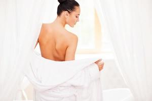 Taking off her bathrobe. Rear view of beautiful young woman taking off her bathrobe while standing in front of bathtub photo