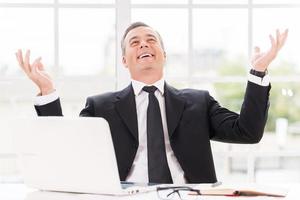 Confident and successful. Happy mature man in formalwear smiling and gesturing while sitting at his working place photo