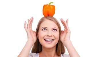 Having fun while cooking. Playful young woman with salad pepper on her head looking up while standing against white background photo