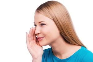 Sharing good news. Side view of beautiful young woman whispering and holding hand near mouth while standing against white background photo