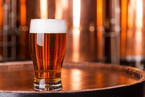 cerveza fresca primer plano de vidrio con cerveza de pie en el barril de madera con recipientes de metal en el fondo