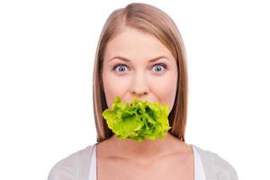 Playful cooker. Excited young woman holding leaf of cabbage in mouth and staring at camera while standing against white background photo
