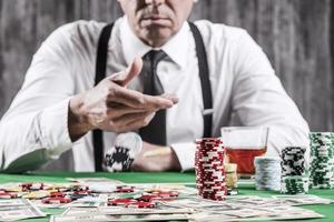 Confident in his luck. Close-up of senior man in shirt and suspenders throwing his gambling chips at the poker table photo