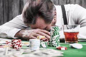 It is not my day. Depressed senior man in shirt and suspenders leaning his head at the poker table with money and gambling chips laying all around him photo