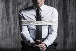 Fear and hopelessness. Cropped image of tied up businessman sitting at the chair with dirty wall  in the background photo