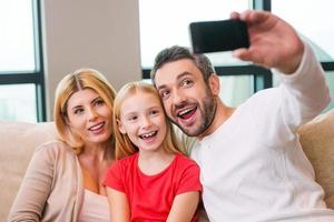 Capturing a bright moment together. Happy family of three bonding to each other and smiling while father photographing them with smart phone photo