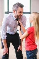 Now you are ready to go. Playful little girl helping father to tie a necktie photo