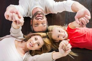 familia feliz juntos. vista superior de la familia feliz de tres que se unen entre sí y sonríen mientras están acostados en el piso de madera dura foto