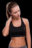 Pain in muscles. Frustrated young woman touching her neck and keeping eyes closed  while standing against black background photo