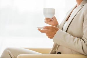 Taking time for coffee break. Side view of businesswoman in suit drinking coffee and looking away while sitting at the chair photo