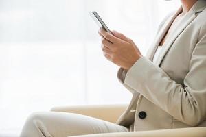Typing business message. Side view of businesswoman in suit typing something on mobile phone while sitting at the chair photo