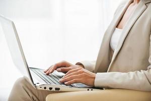 Working on laptop. Side view of young businesswoman in suit working on laptop while sitting at the chair photo