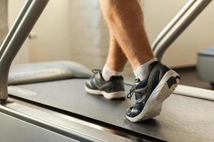 Exercising on treadmill. Close-up of man walking by treadmill in sports club photo