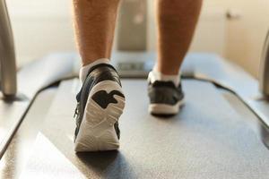 Walking on treadmill. Close-up of man walking by treadmill in sports club photo