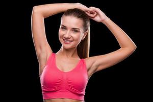 Sporty beauty. Sporty young woman keeping arms raised and smiling while standing against black background photo