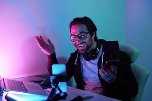 Handsome young man smiling and gesturing while streaming online against colorful background photo