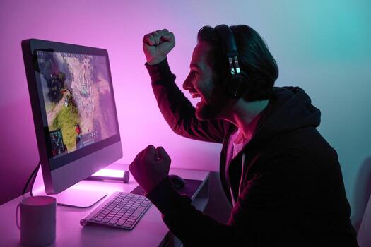 Side view of happy man gesturing while playing computer game against colorful background photo