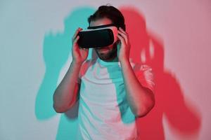Confident young man adjusting his virtual reality eyeglasses with colorful shadows in the background photo