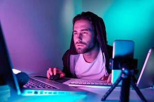 Confident young man using computer during live stream against colorful background photo