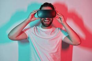 Happy young man adjusting his virtual reality eyeglasses with colorful shadows in the background photo