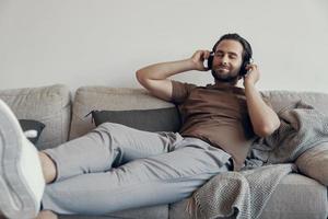 Handsome young man adjusting his headphones while relaxing on the couch at home photo